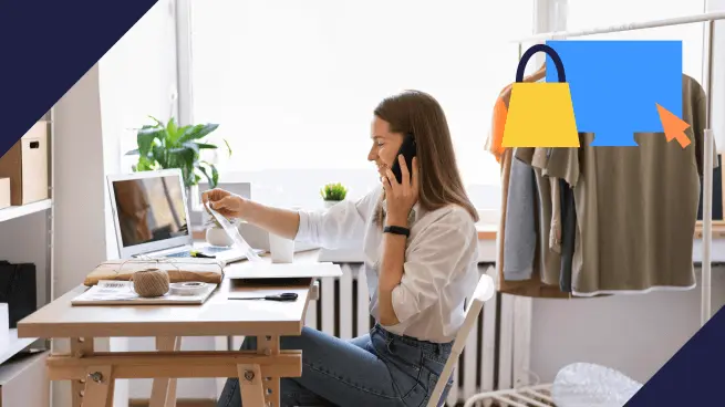 Mulher sentada à mesa, falando ao telefone e segurando papéis enquanto olha para o laptop. Ao fundo, há roupas penduradas e itens de escritório. Um ícone de sacola de compras aparece no canto superior direito.