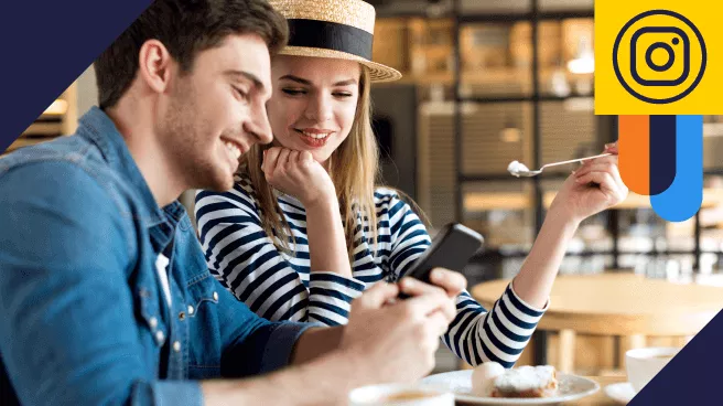 Um jovem casal em um café compartilha um momento alegre. Ele, vestido casualmente, mostra algo no smartphone à mulher ao seu lado, que sorri enquanto observa a tela. Ambiente aconchegante ao fundo.