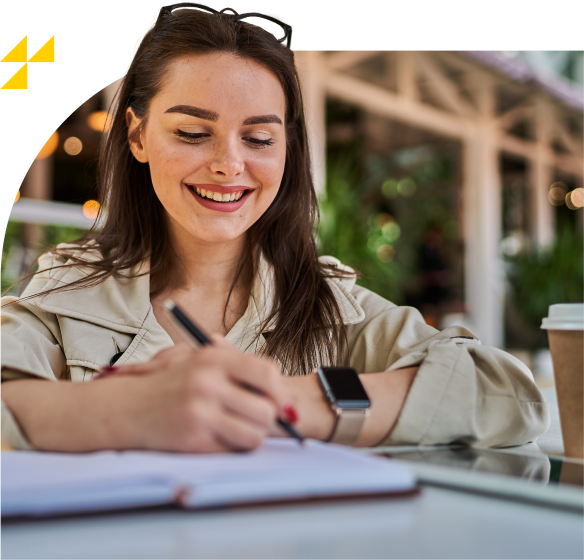 Mulher sorridente escrevendo em um caderno enquanto está sentada ao ar livre. Ela usa óculos de sol sobre a cabeça e um smartwatch no pulso. Uma xícara de café descartável está ao lado. Ícone amarelo aparece no canto superior esquerdo.